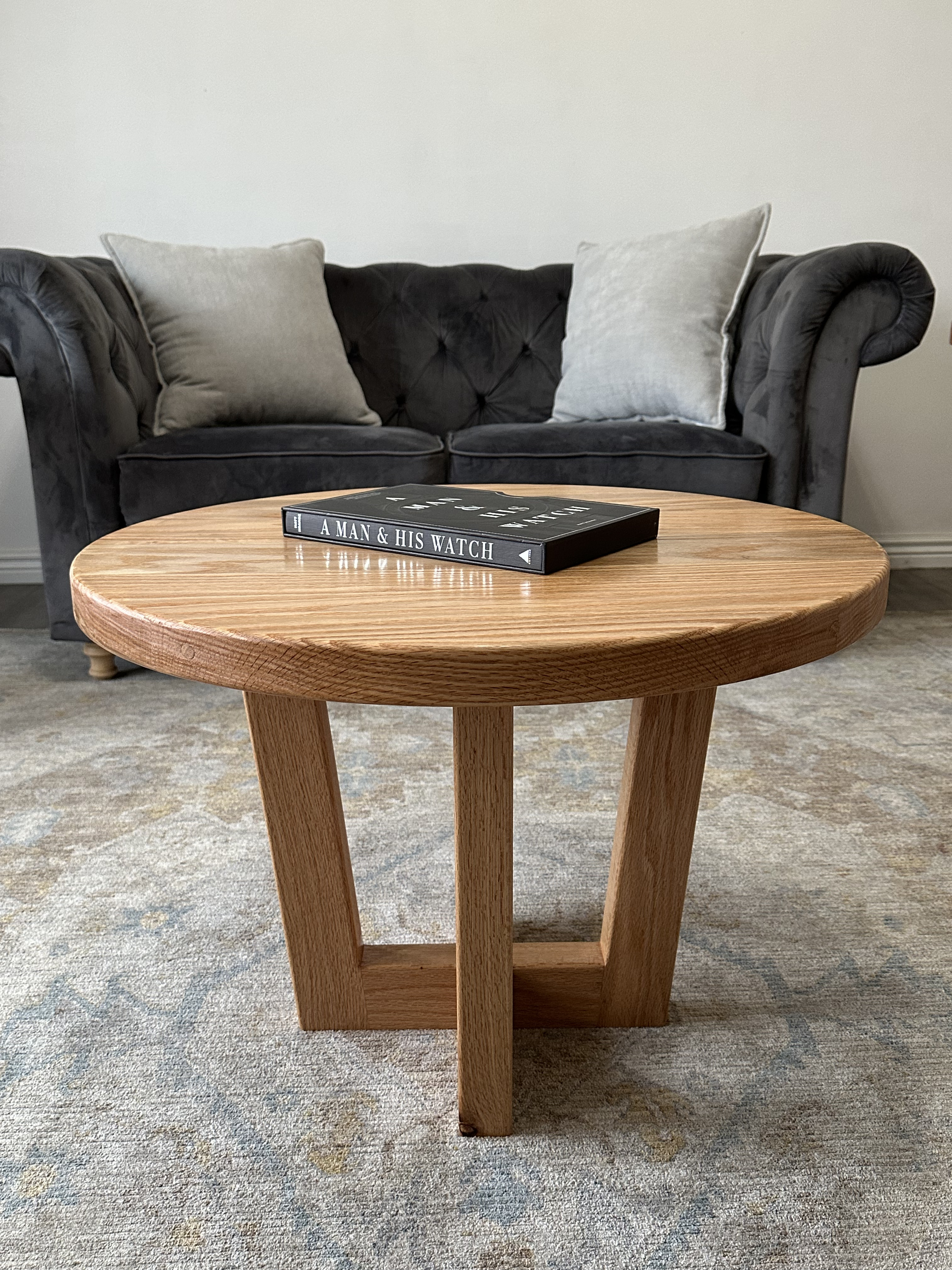 Round oak coffee table with cross-base design and book styled on top