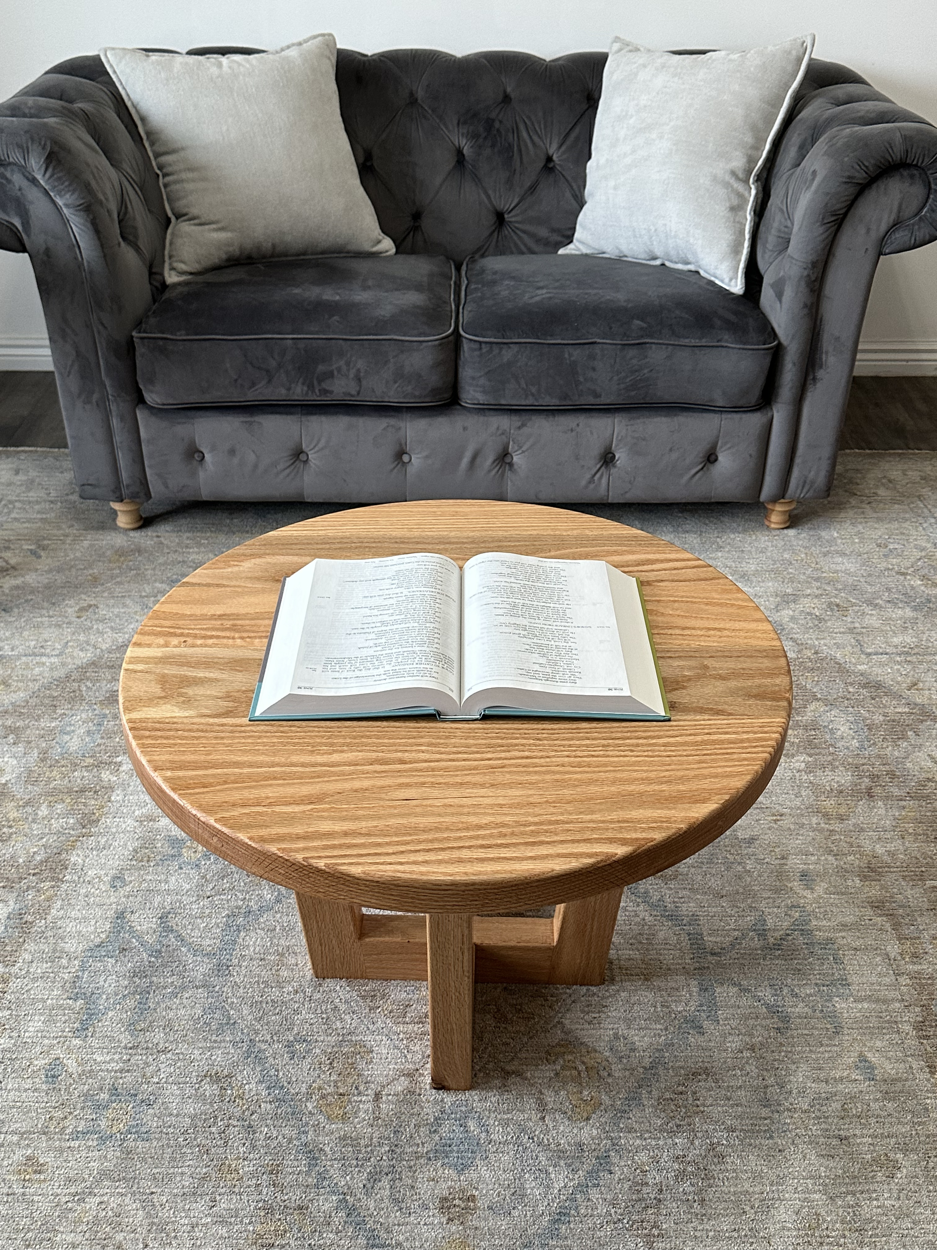 Round oak coffee table in living room setting with open book  - lifestyle shot